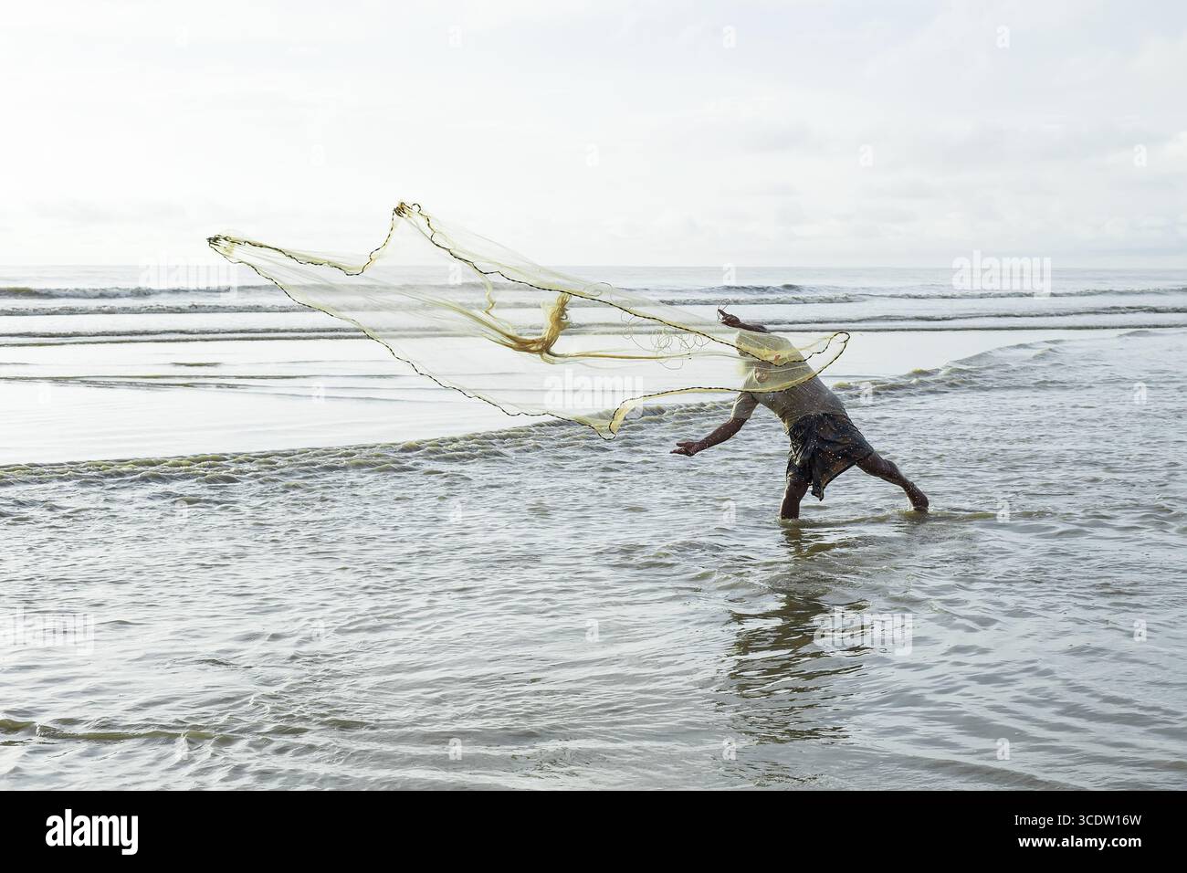 Cox's Bazar, Bangladesh - 11 octobre 2019 : vue d'un pêcheur jetant un filet dans l'eau chatoyante et ensoleillée le long de la plage de sable. Banque D'Images