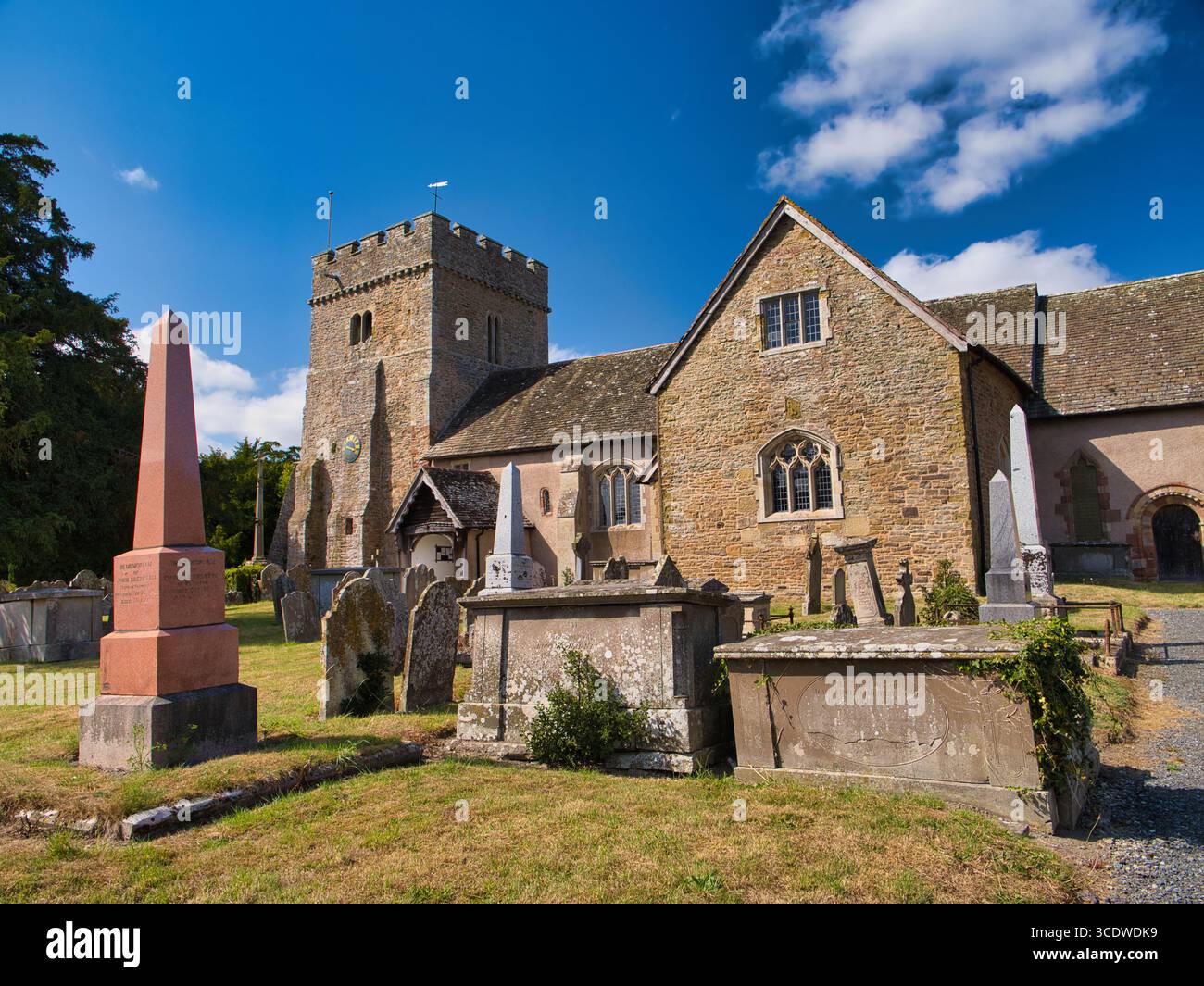 Lydbury North, Royaume-Uni - août 08 2025 : St Michael & All Angels, une église du 12ème siècle classée Grade I à Lydbury North, Shropshire, Royaume-Uni, avec une tour crénelée et des tombes historiques sous un ciel d'été lumineux. Banque D'Images