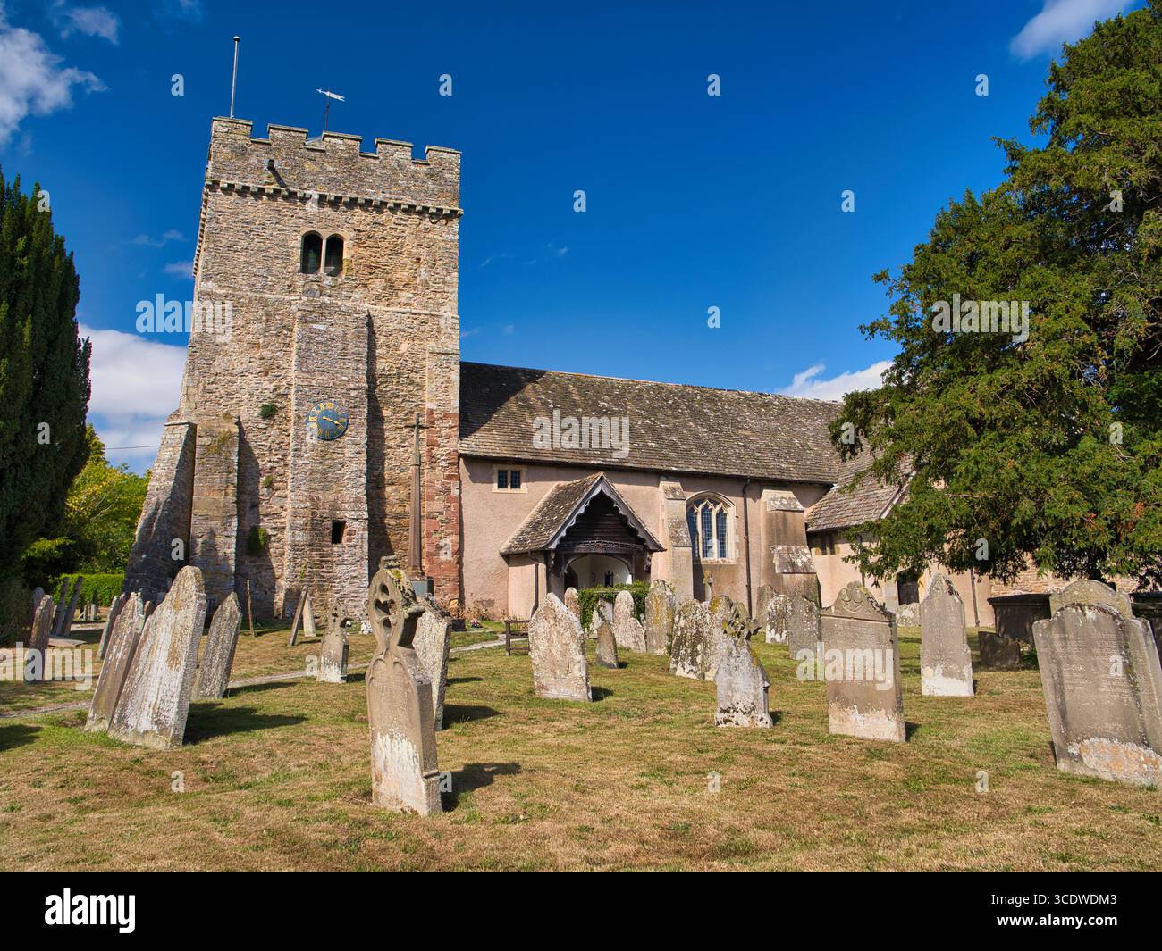 Lydbury North, Royaume-Uni - août 08 2025 : 12ème siècle St Michael & All Angels, une église paroissiale classée Grade I à Lydbury North, Shropshire, Angleterre, encadrée par des pierres tombales altérées sous un ciel d'été lumineux. Banque D'Images