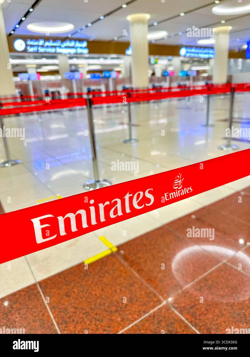 Zone d'enregistrement vide à l'aéroport avec ruban adhésif rouge Emirates et bornes libre-service en arrière-plan au terminal DXB 3 de Dubaï - Image de stock capturée avec un smartphone
