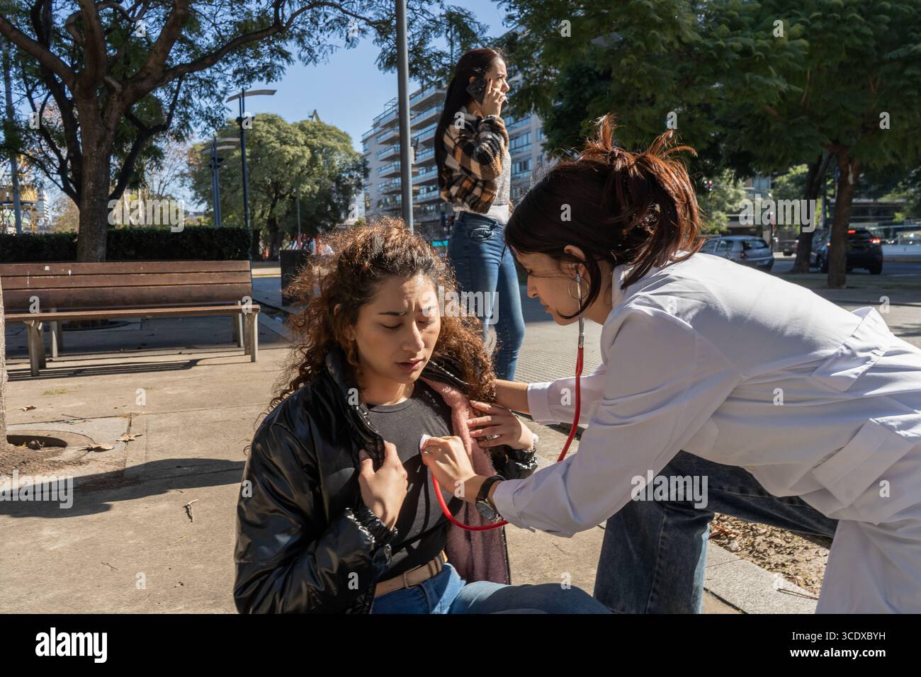 Médecin examinant une jeune femme dans une rue de la ville, à l'aide d'un stéthoscope pour vérifier son rythme cardiaque Banque D'Images