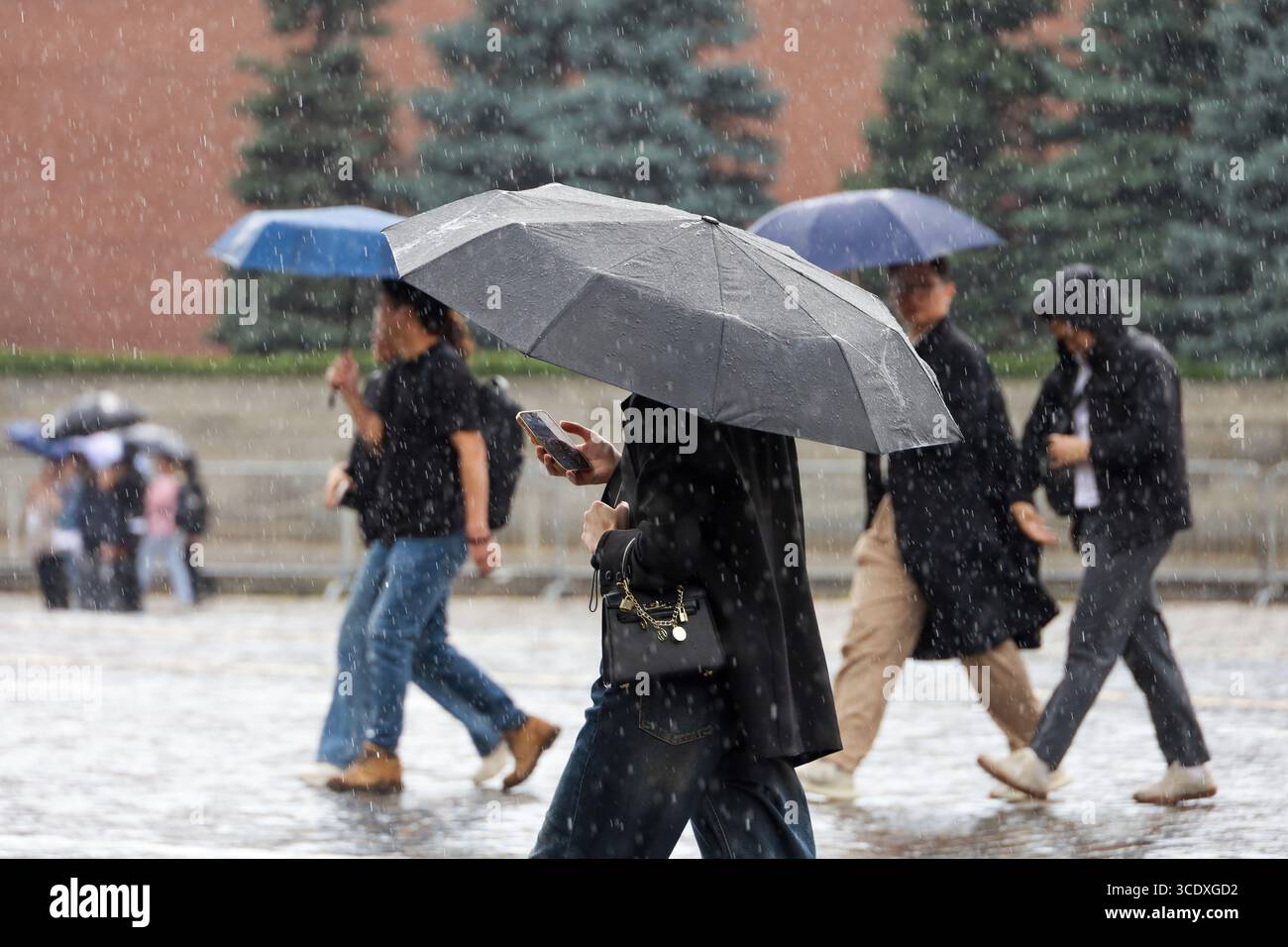 Personnes avec des parapluies marchant sur la place Rouge à Moscou, femme avec smartphone au premier plan. Fortes pluies en ville en été Banque D'Images