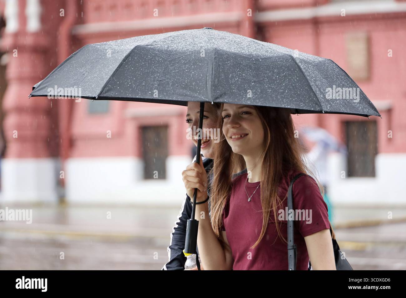 Deux filles heureuses avec un parapluie marchant dans une rue. Fortes pluies en ville en été Banque D'Images