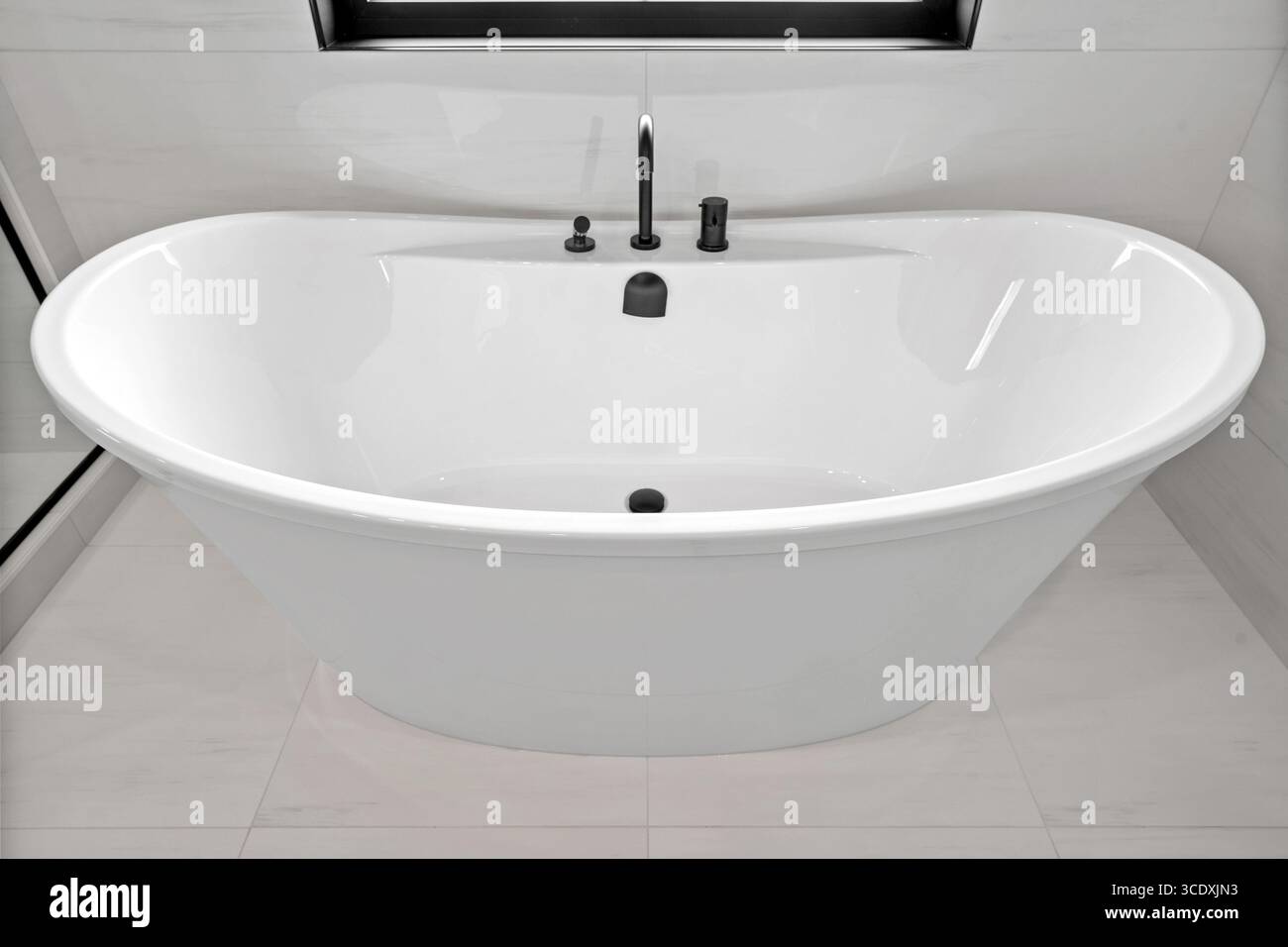 Grande baignoire blanche avec robinet noir. La baignoire est propre et brillante, et le robinet noir ajoute une touche d'élégance à la salle de bain Banque D'Images