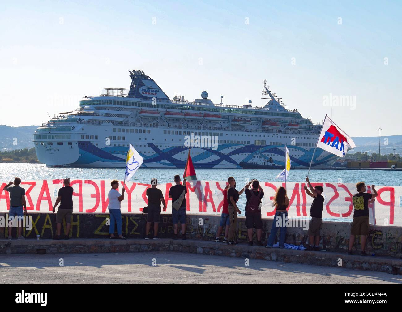Volos, Grèce, 13 août 2025. Les manifestants tiennent des banderoles et des drapeaux lors d'une manifestation dans le port de Volos, alors que le navire de croisière israélien Crown Iris, visible à l'arrière-plan, part. Des manifestations ont eu lieu sur les îles grecques et les ports continentaux le long de la route de l'Iris de la Couronne, qui transporterait des soldats israéliens en vacances en Grèce. Crédit : Dimitris Aspiotis/Alamy Live News Banque D'Images