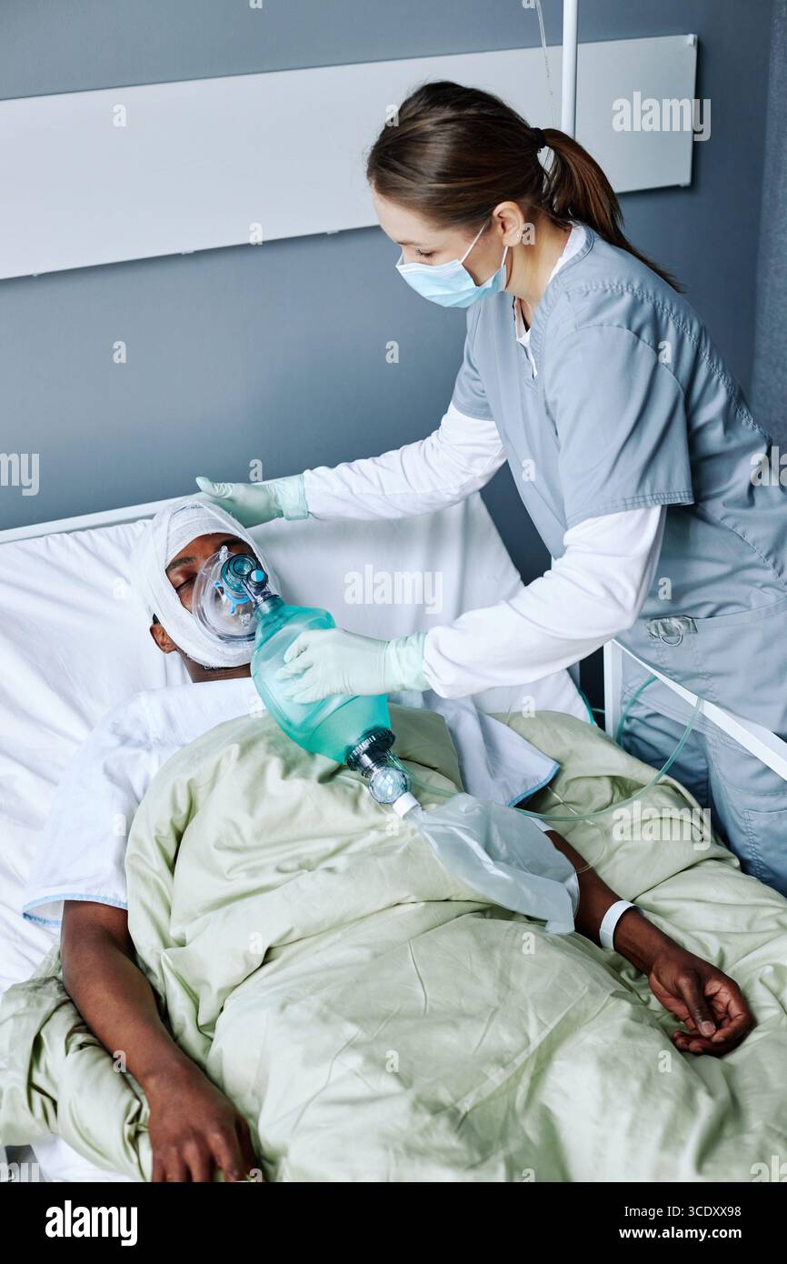 Vue verticale en grand angle d'une infirmière caucasienne portant un masque sur le visage en ventilation artificielle pour un jeune homme noir blessé Banque D'Images