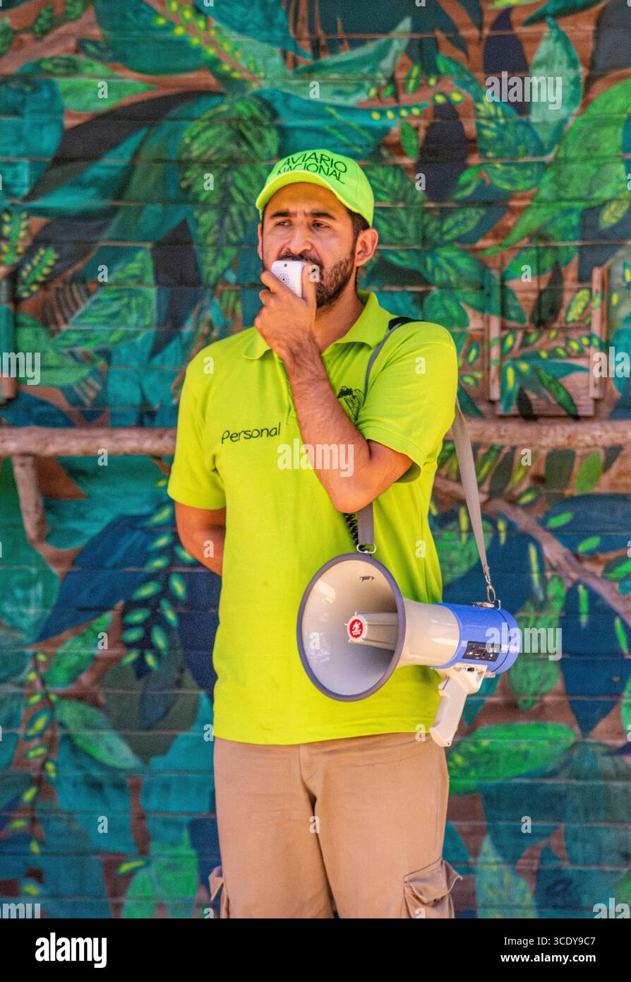 Un guide masculin communique avec les invités à l'aide d'un mégaphone à l'Aviario Nacional de Cartagena, entouré d'un feuillage tropical vibrant. Banque D'Images