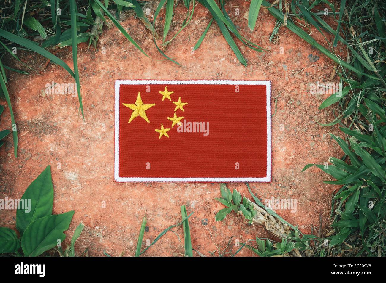Drapeau chinois brodé sur une pierre rustique avec de l'herbe verte, symbolisant l'éco-tourisme, la sensibilisation à l'environnement et le changement climatique. Banque D'Images