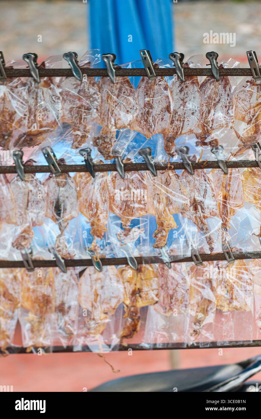 Étal de marché nocturne thaïlandais avec calmars séchés coupés sur une grille, scellés dans des sacs transparents, mettant en valeur la culture culinaire de rue authentique et la tradition culinaire. Banque D'Images