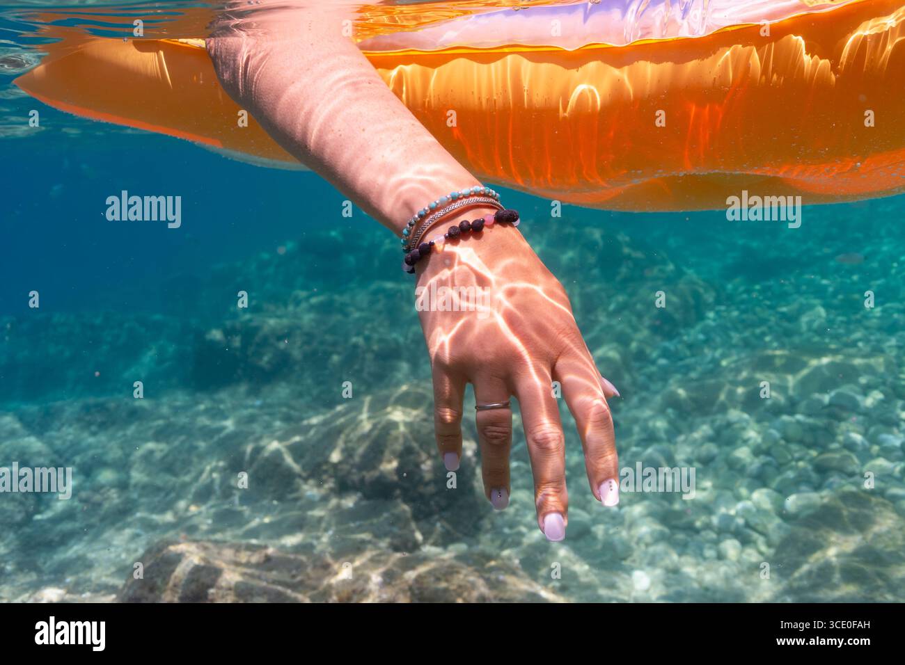 La main de la femme avec des bracelets plonge dans l'eau de mer claire avec des caustiques solaires tout en se relaxant sur un flotteur gonflable. Banque D'Images