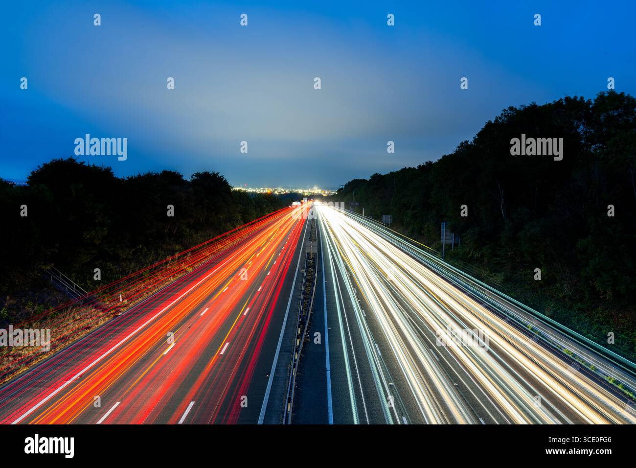Longue exposition de voitures conduisant sur l'autoroute au crépuscule créant des traînées lumineuses avec les lumières de la ville en arrière-plan Banque D'Images