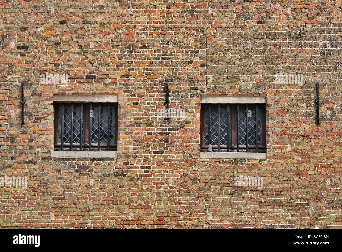Vieux mur de briques avec deux fenêtres barrées, design symétrique et texture rustique, partie d'une façade de bâtiment historique. Banque D'Images