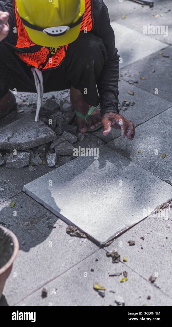 Un travailleur âgé répare des sols en pierre naturelle à Manahan, Surakarta, mettant en valeur les compétences traditionnelles et la précision dans les travaux de construction. Banque D'Images