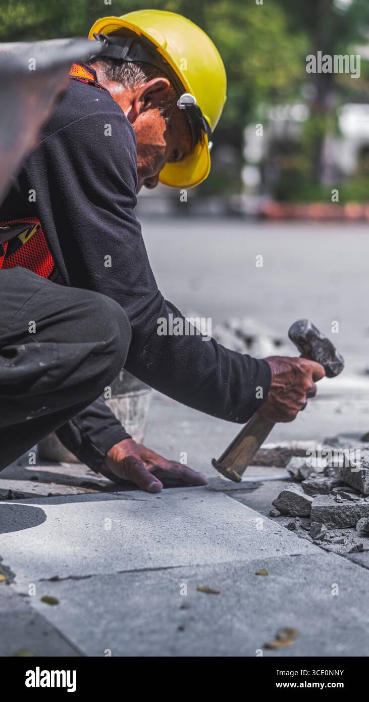 Un travailleur âgé répare des sols en pierre naturelle à Manahan, Surakarta, mettant en valeur les compétences traditionnelles et la précision dans les travaux de construction. Banque D'Images