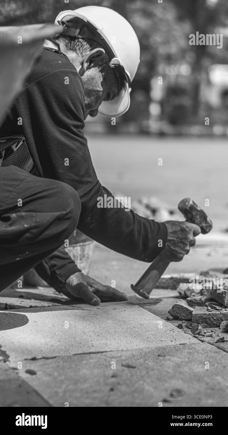 Un travailleur âgé répare des sols en pierre naturelle à Manahan, Surakarta, mettant en valeur les compétences traditionnelles et la précision dans les travaux de construction. Banque D'Images