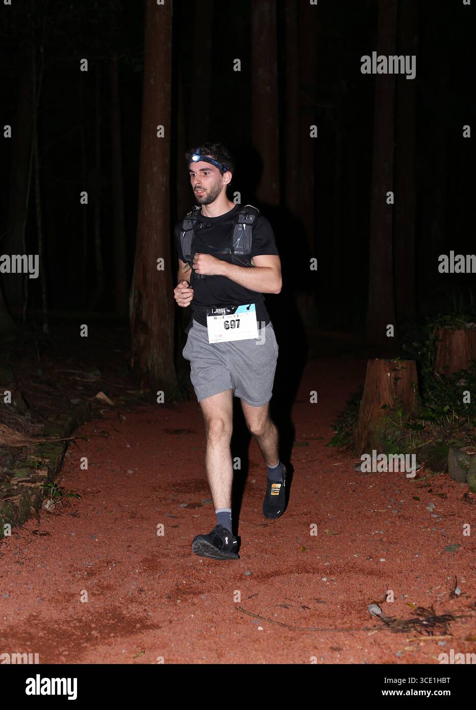 Les coureurs éclairent le sentier forestier avec des phares lors de l’événement Furnas Night Trail, combinant endurance et aventure nocturne. Banque D'Images