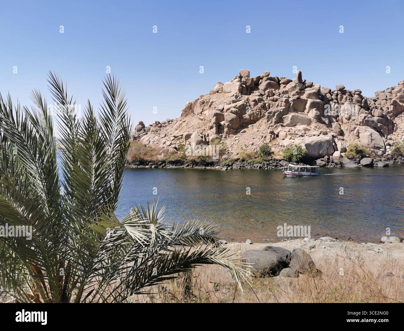 Tourist Boat passe devant de grandes îles de granit près de Philae Temple, Assouan, partiellement submergées par la montée des eaux du Nil du barrage britannique. - Image de stock capturée avec un smartphone