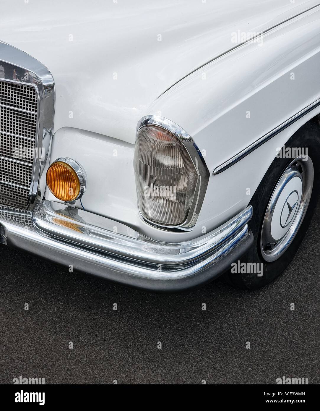 Coin avant gauche de la vieille Mercedes blanche des années 1960. Voiture classique dans le parking - vue rapprochée du phare, de la calandre, du phare antibrouillard, de l'aile, du capot de pare-chocs et de la roue. Banque D'Images