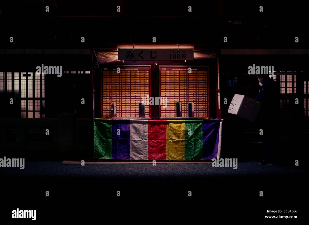 Ouvrier portant une boîte à côté du stand de fortune omikuji illuminé au temple Sensō-ji à Asakusa, pendant la nuit Banque D'Images