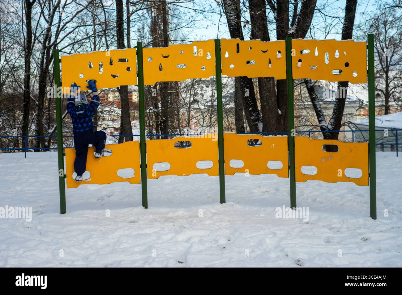 05.11.2016, Tartu, Estonie : enfant grimpant structure de jeu jaune dans une aire de jeux enneigée. Banque D'Images