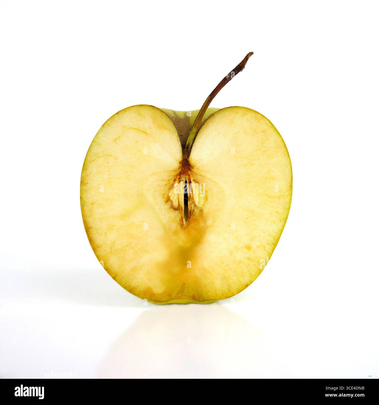 Une pomme coupée en deux montre sa chair jaunâtre avec des taches brunes, reposant sur une surface réfléchissante. La coupe révèle les graines et la texture Banque D'Images