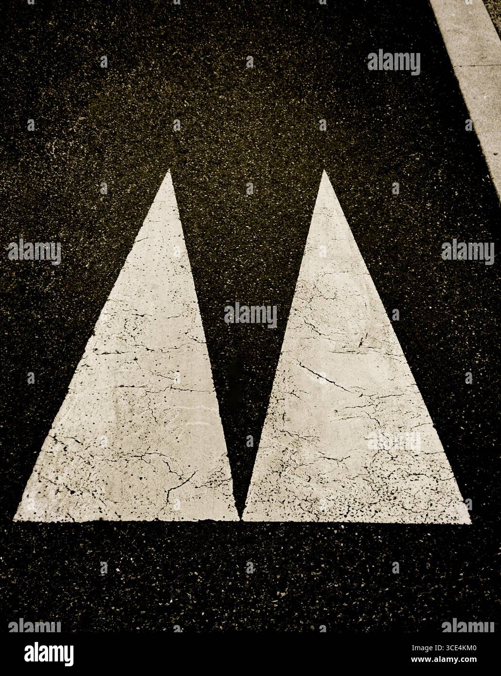 Deux grandes marques triangulaires en peinture blanche se détachent contre l'asphalte foncé, mettant en évidence l'usure. Banque D'Images
