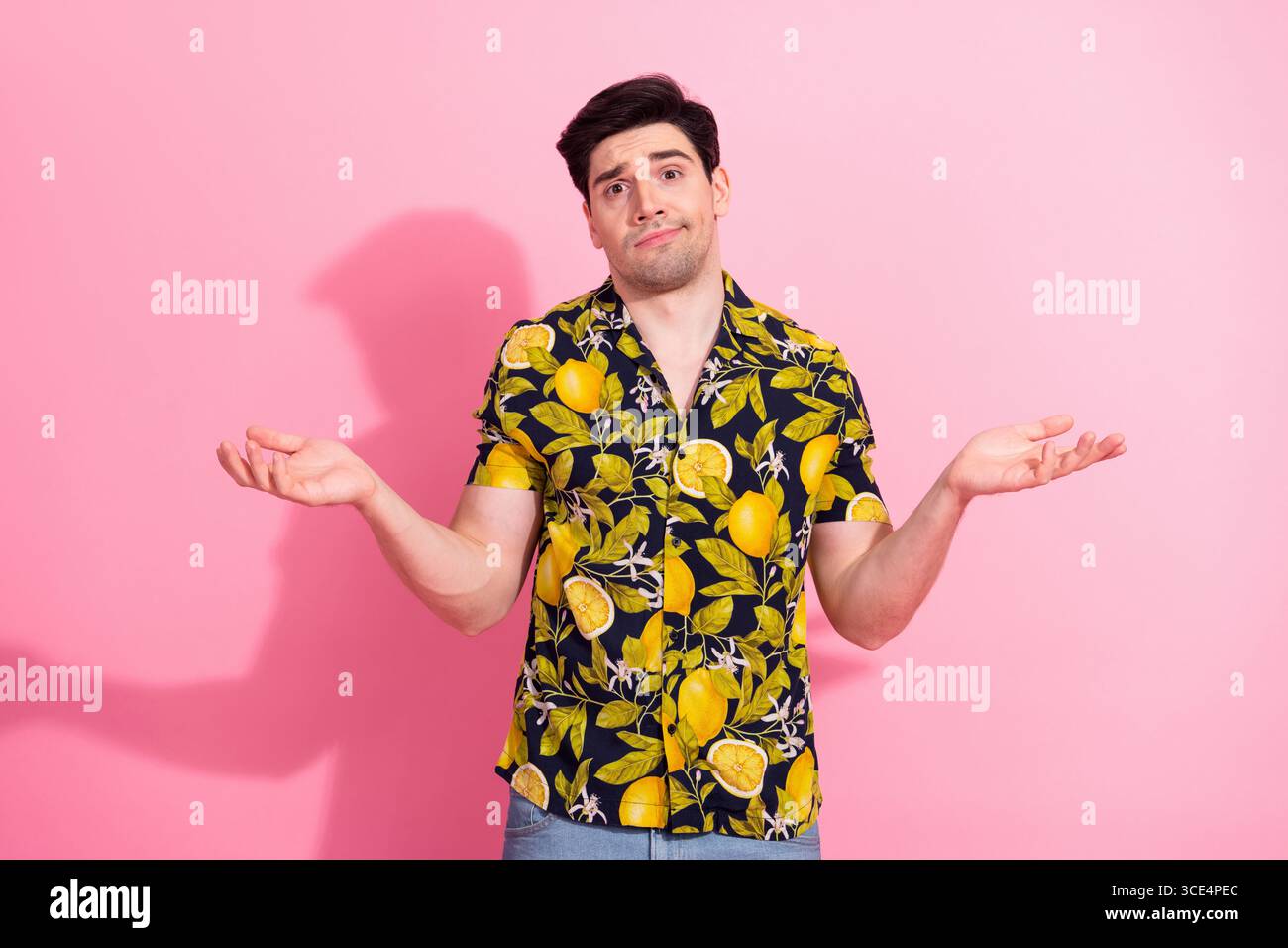 Jeune homme dans une chemise tropicale faisant des gestes avec une expression perplexe sur un fond rose Banque D'Images