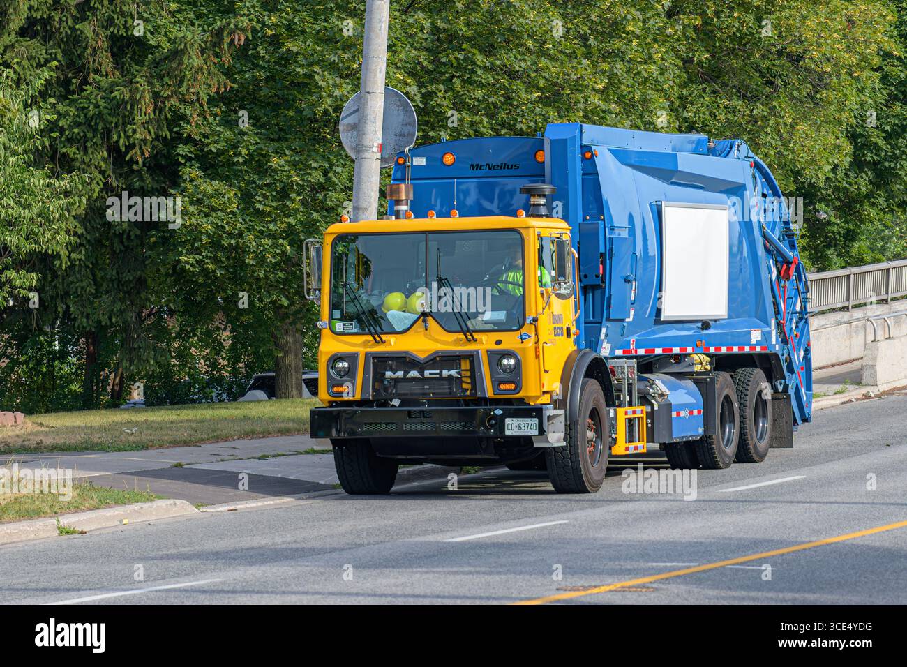 Un camion de collecte des déchets de la ville de Toronto longe une route résidentielle, arborant un taxi jaune et une carrosserie McNeilus bleue. Banque D'Images