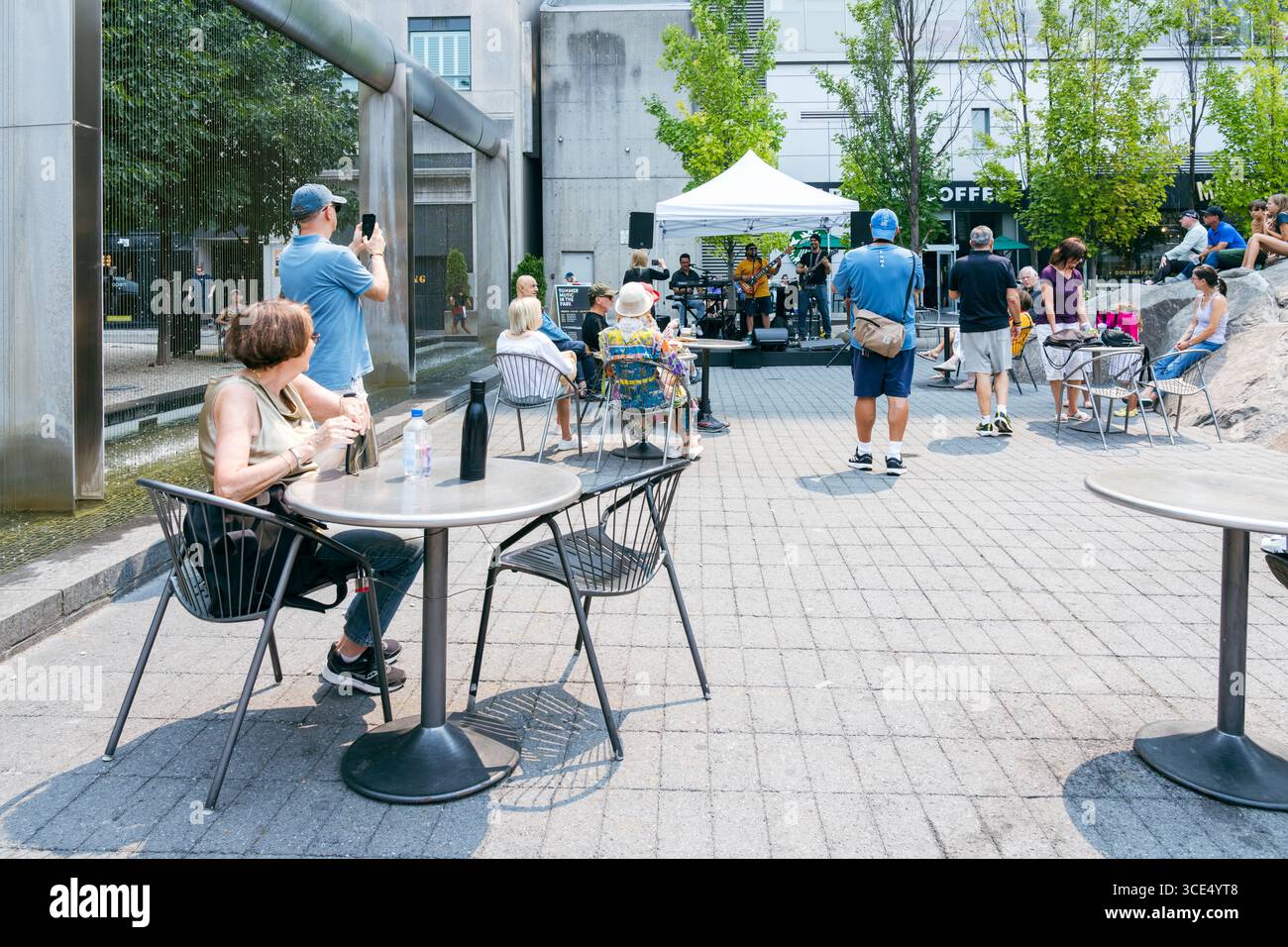 Les gens s'assoient et se tiennent debout près de tables en regardant un groupe en direct se produire sous un auvent dans une place publique à Yorkville. Banque D'Images