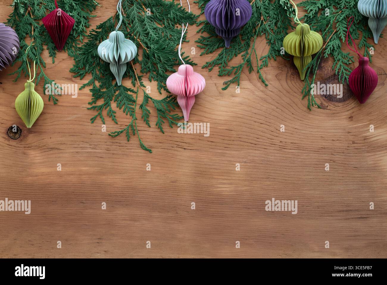 Ornements de noël en papier nid d'abeille multicolore diy accrochés au sommet du cadre avec des branches vertes sur fond de bois et espace de copie Banque D'Images