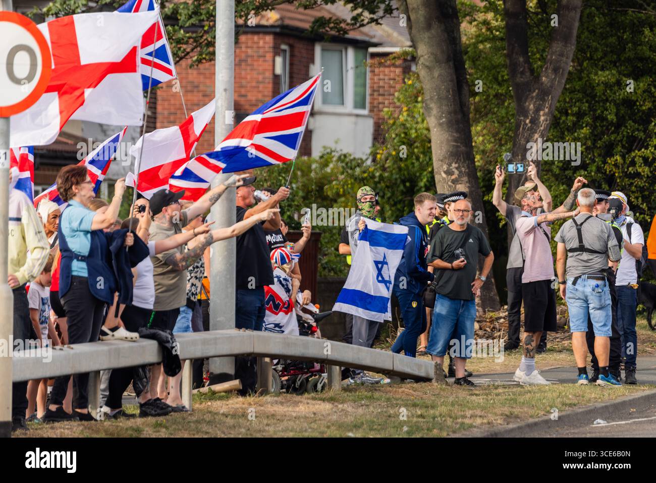 Leeds, Royaume-Uni. 15 AOÛT 2025. Les manifestants tiennent les drapeaux de l'Angleterre et de l'Union Jack de l'autre côté comme pour la quatrième semaine consécutive, des groupes opposés de manifestants pro et anti-migrants se sont rassemblés sur le bord de la route près de l'hôtel Britannia à Seacroft, Leeds. Les manifestants de 'Stand Up Leeds' ont déclenché de multiples fusées éclairantes et trois contre-manifestants ont été arrêtés après des échauffourées entre militants et police. Crédit Milo Chandler/Alamy Live News Banque D'Images