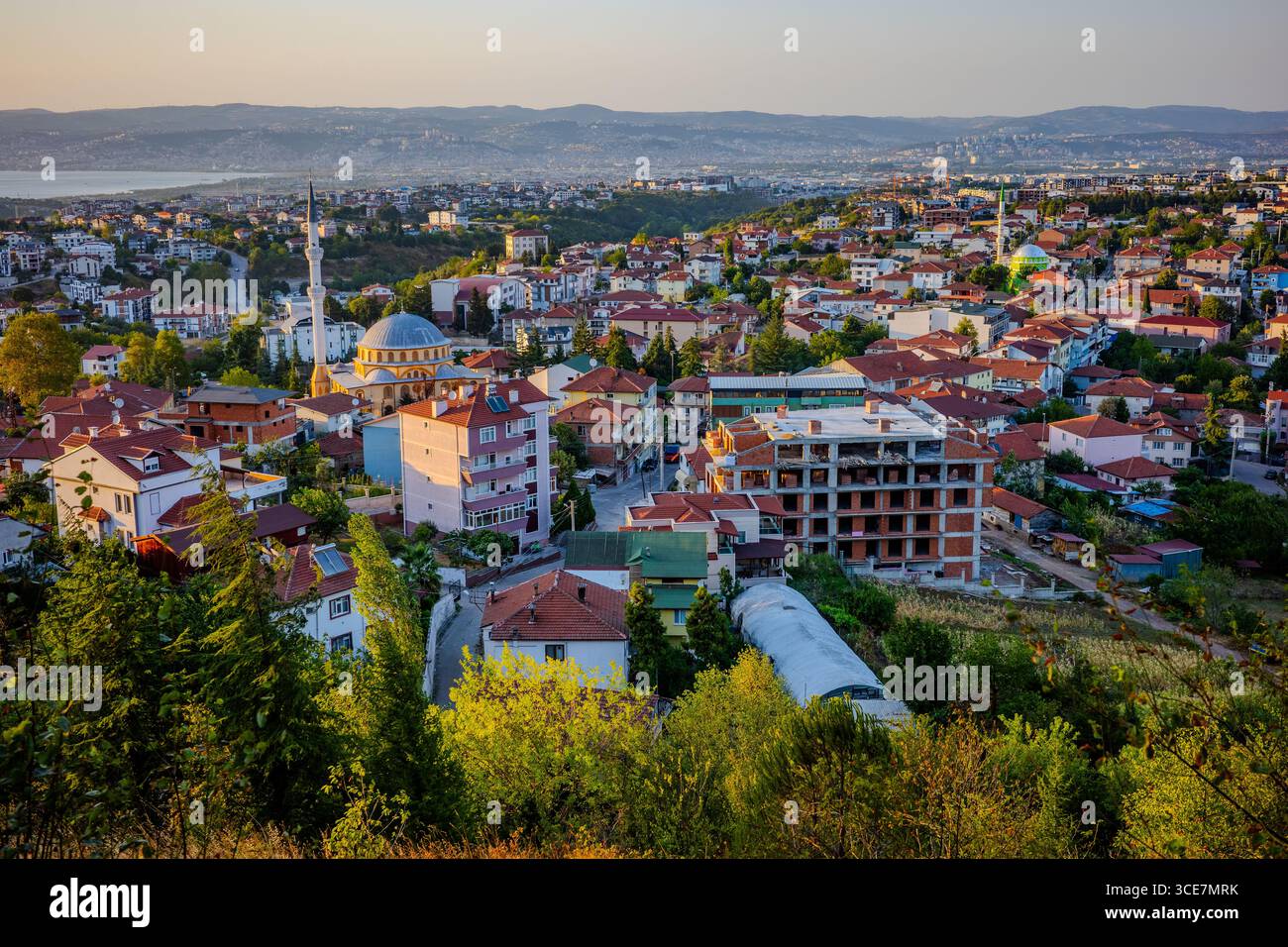 Vue surélevée de Başiskele, Kocaeli, Türkiye au coucher du soleil, avec toits résidentiels, mosquées, chantiers de construction, et le littoral lointain sous Banque D'Images