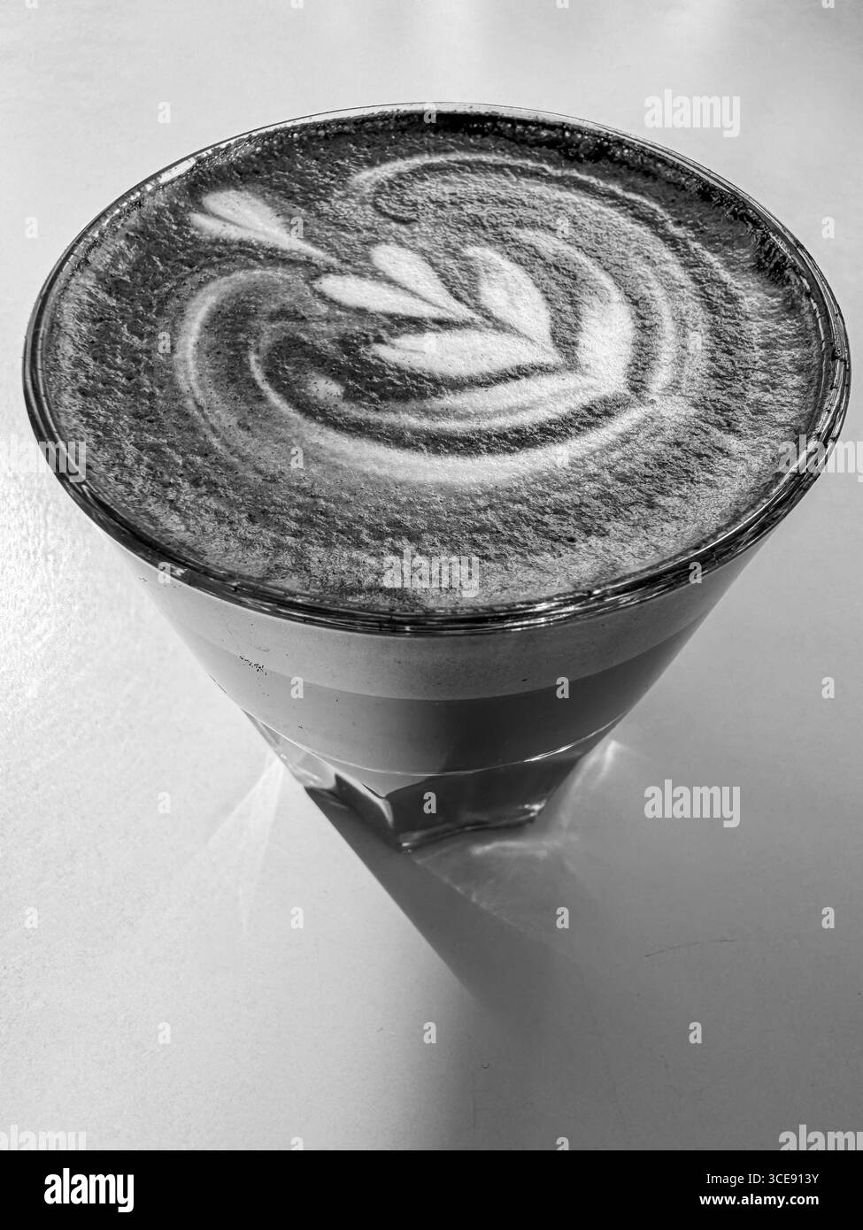 Image en noir et blanc d'un latte avec des œuvres d'art en forme de feuilles complexes, servies dans un verre transparent. L'œuvre tourbillonne magnifiquement, capturant les es Banque D'Images