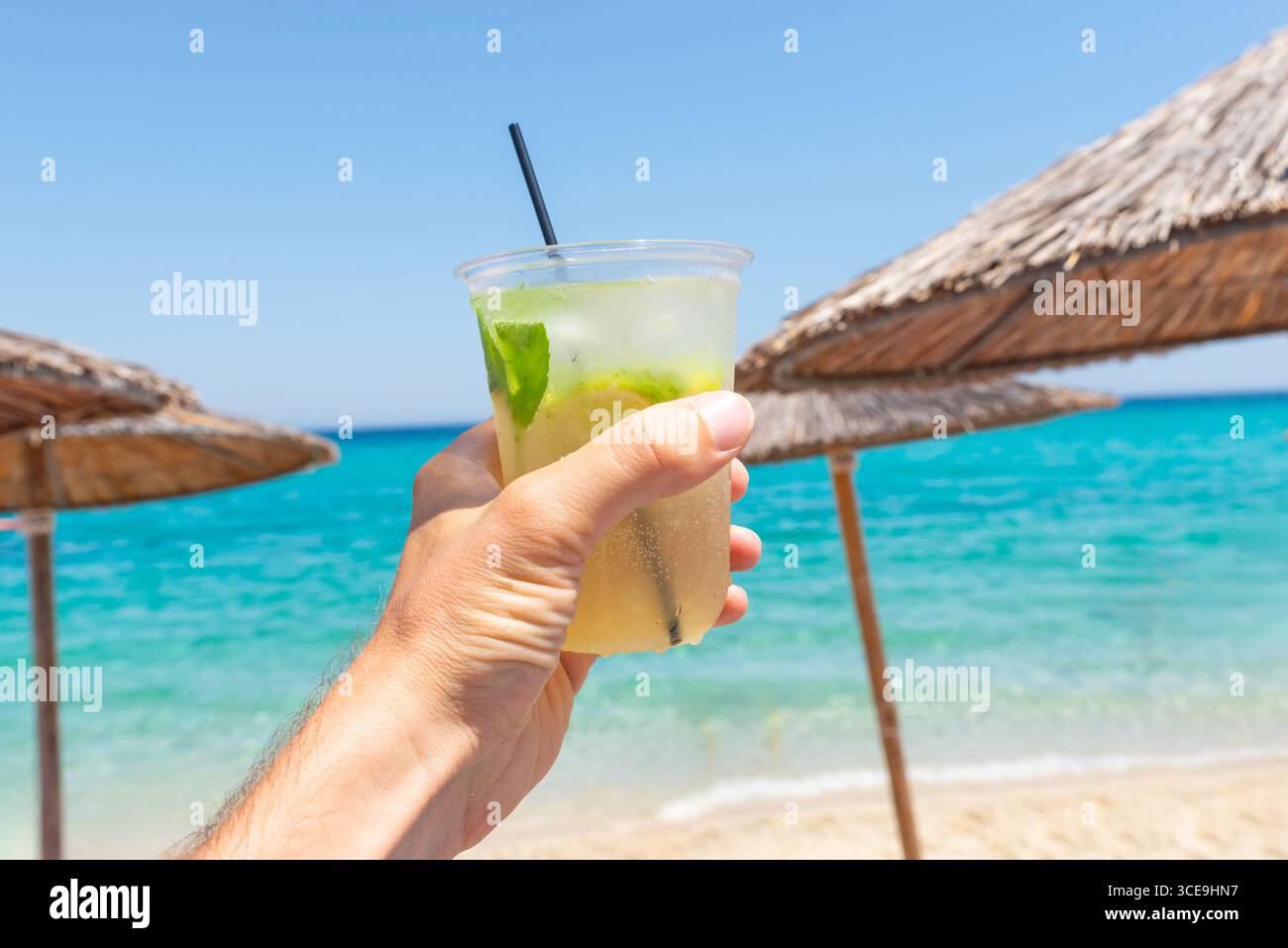 Main tenant cocktail rafraîchissant avec citron vert et menthe sur fond de plage tropicale, parfait pour les concepts d'été et de vacances Banque D'Images
