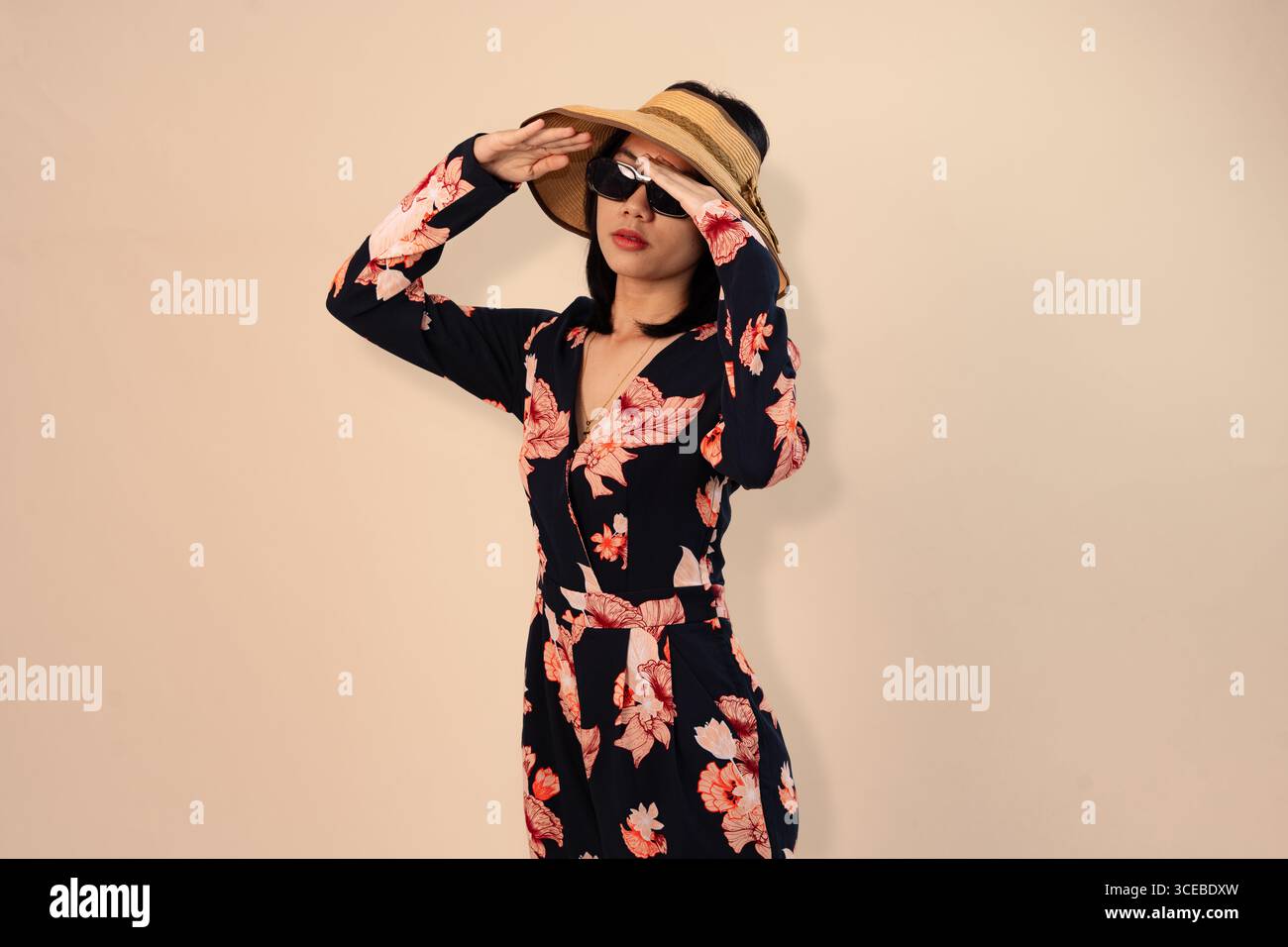femme élégante dans une robe florale et chapeau de paille posant avec style Banque D'Images