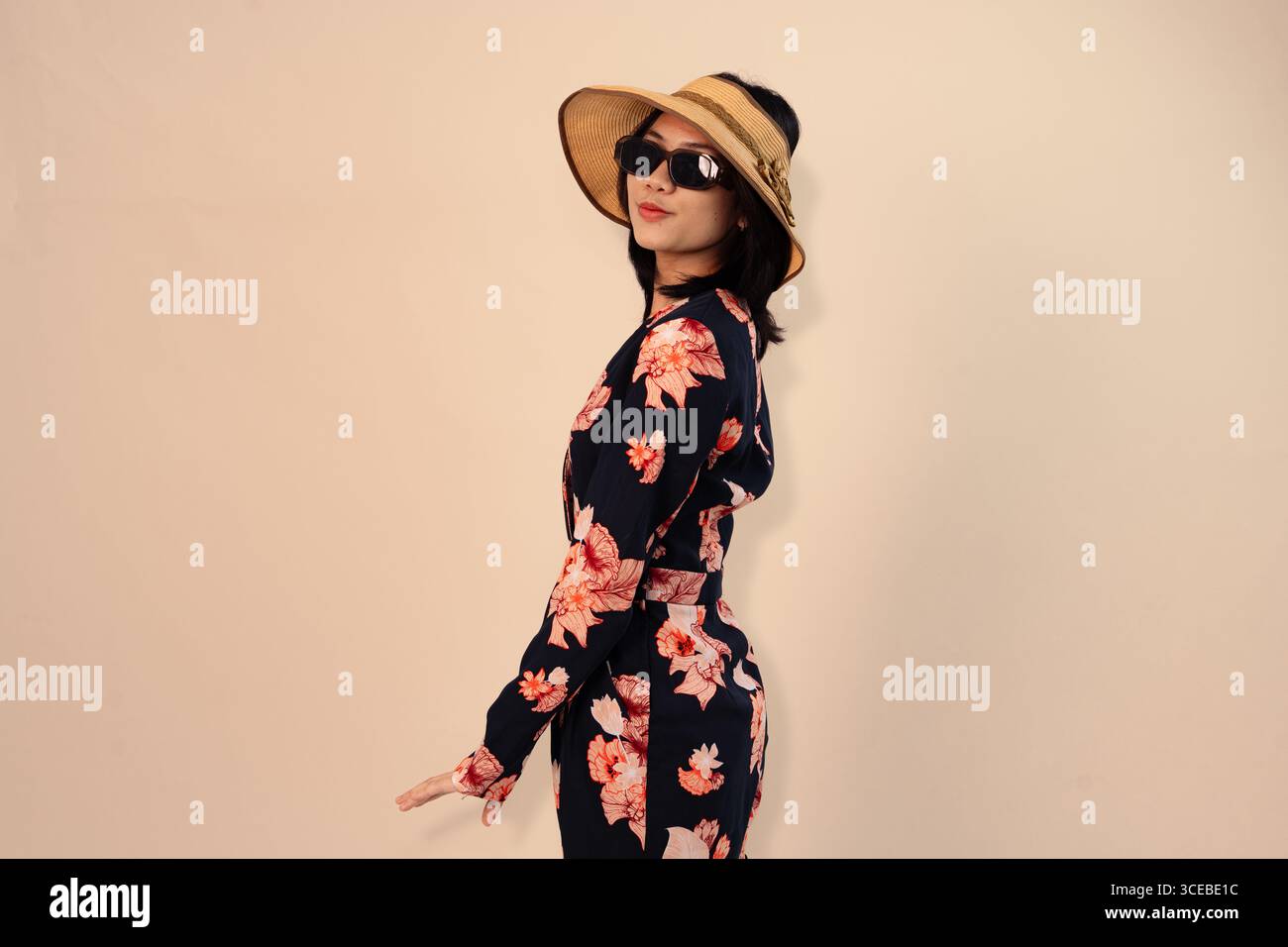 femme élégante dans une robe florale et chapeau de paille posant avec style Banque D'Images
