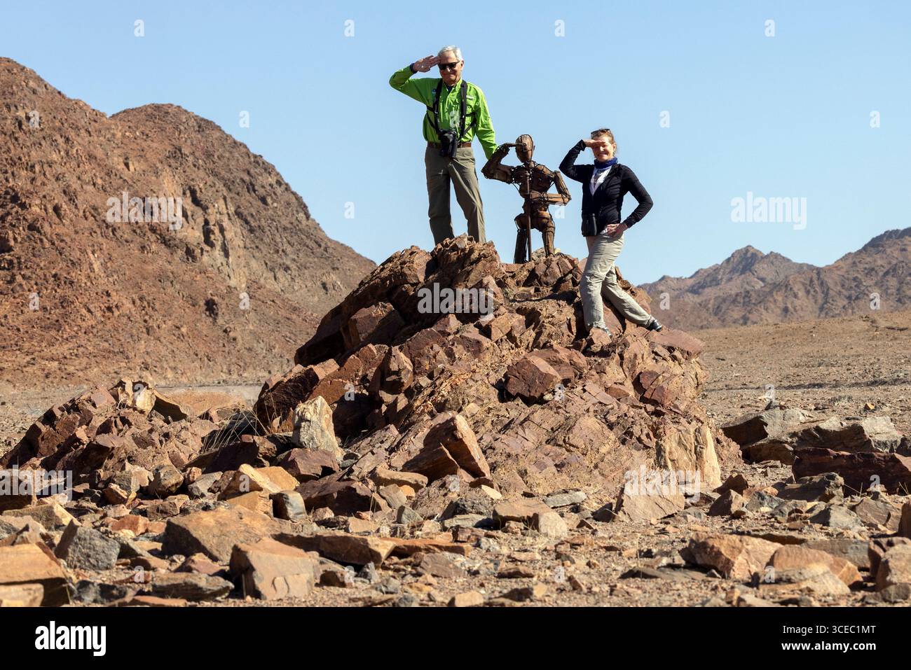Couple posant avec une sculpture 'Lone Stone Men' par l'artiste RENN dans le désert du Namib - région de Kaokoland, Namibie, Afrique Banque D'Images
