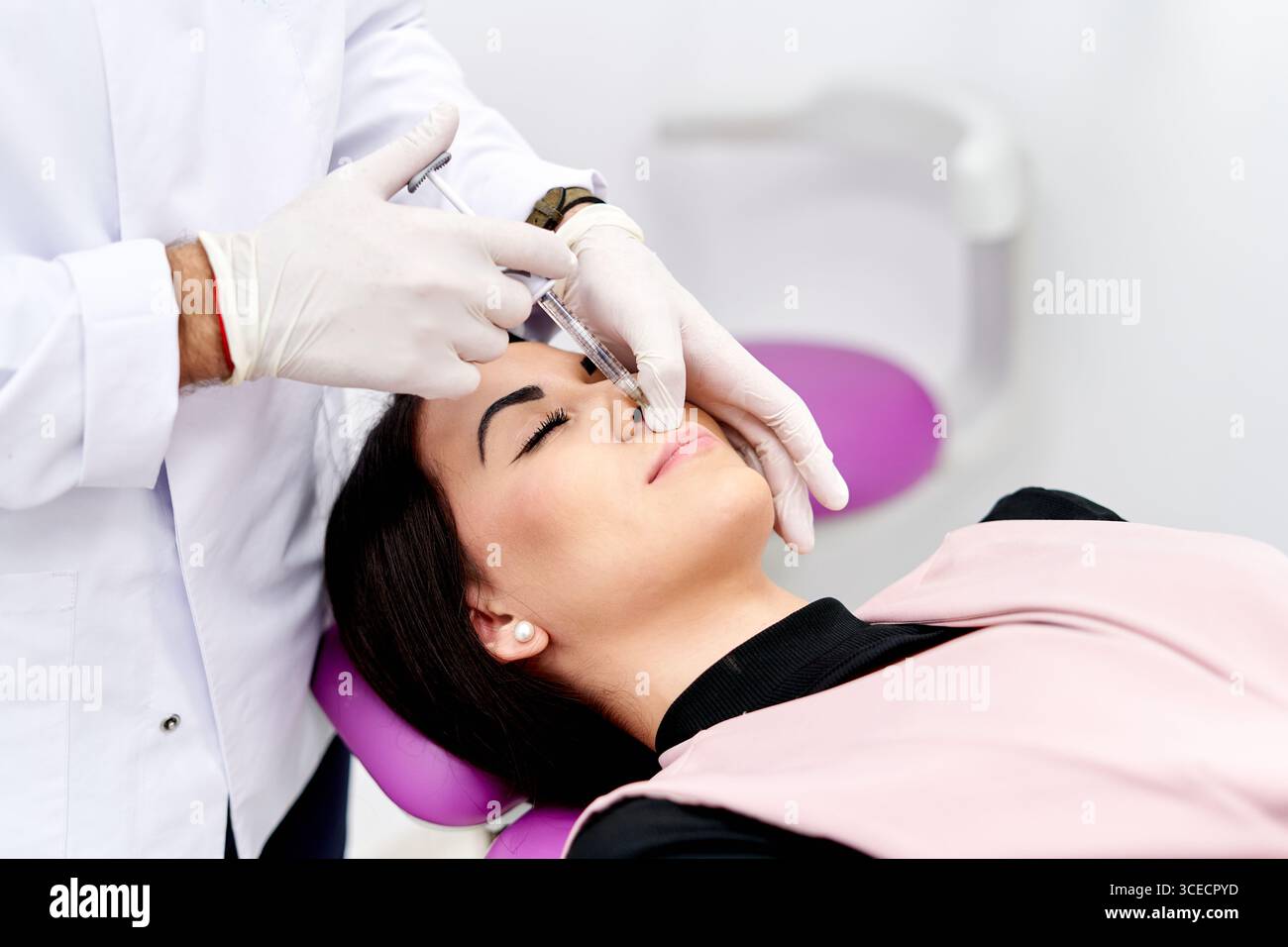 Un professionnel de la santé administre une injection faciale cosmétique à une femme allongée sur une chaise de traitement. L'image capture un environnement serein et stérile Banque D'Images