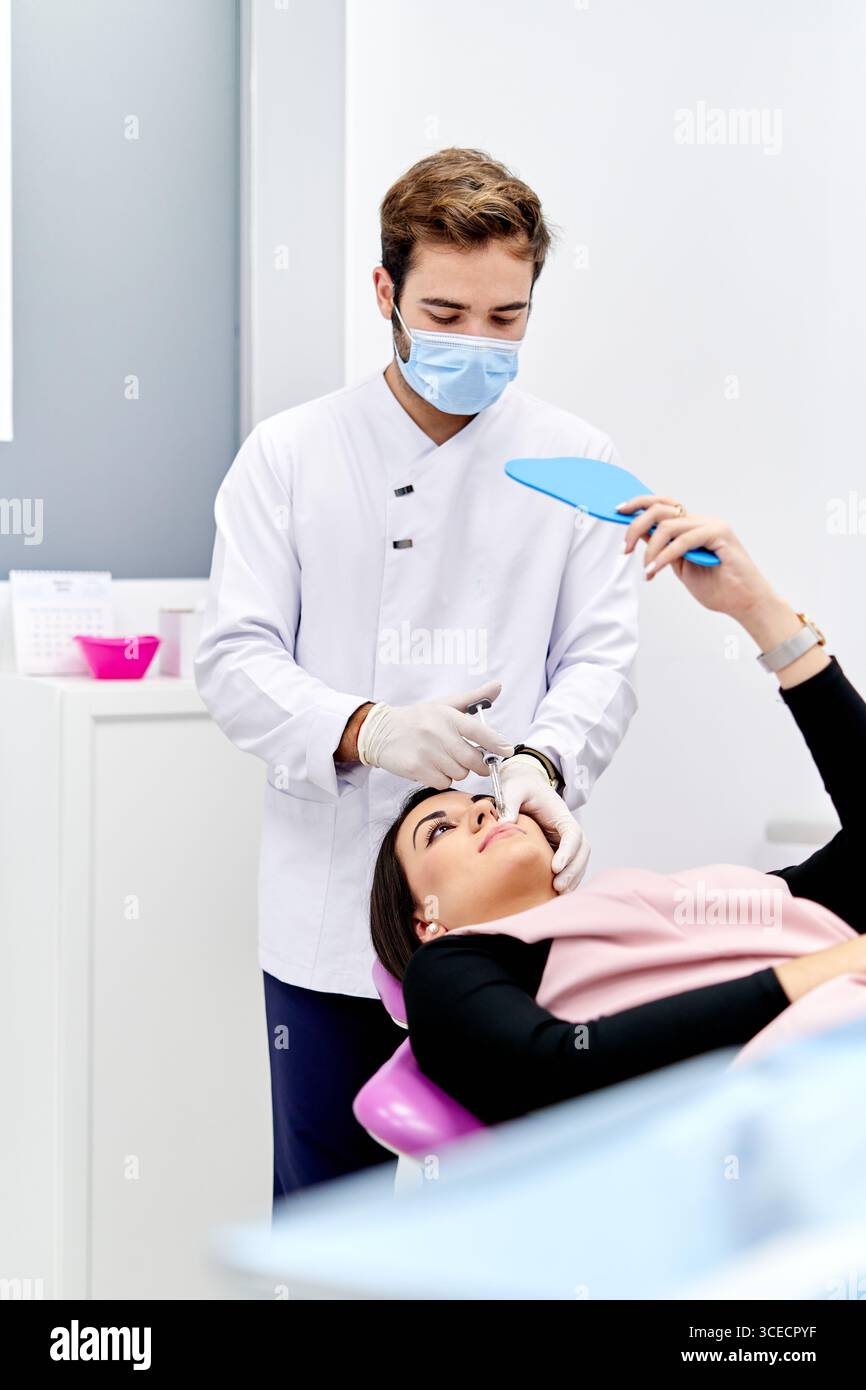 Un médecin dans un cabinet médical administre une injection d'acide hyaluronique à un patient. Le médecin porte un masque et des gants blancs stériles, assurant un nettoyage Banque D'Images