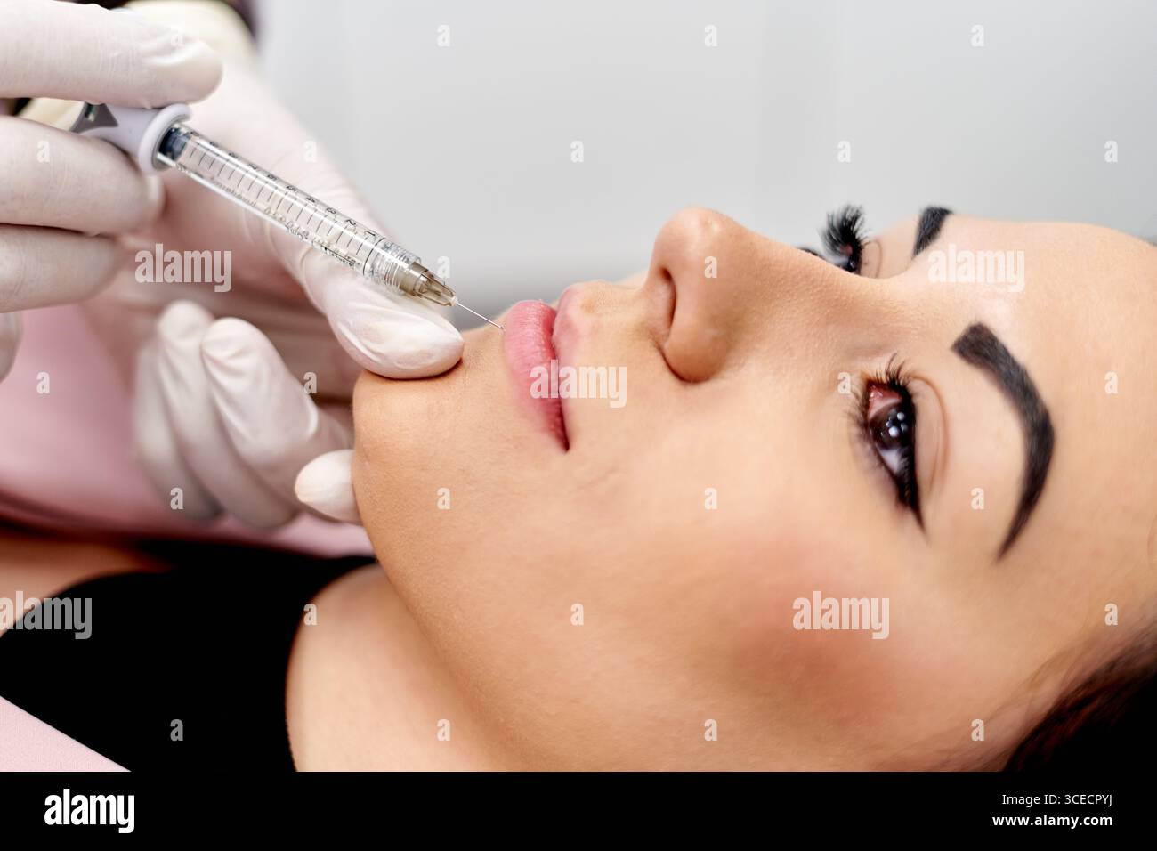 Vue rapprochée d'une procédure cosmétique lorsqu'un spécialiste administre une injection de rehaussement des lèvres à l'aide d'une seringue. Le patient est couché confortablement, showc Banque D'Images