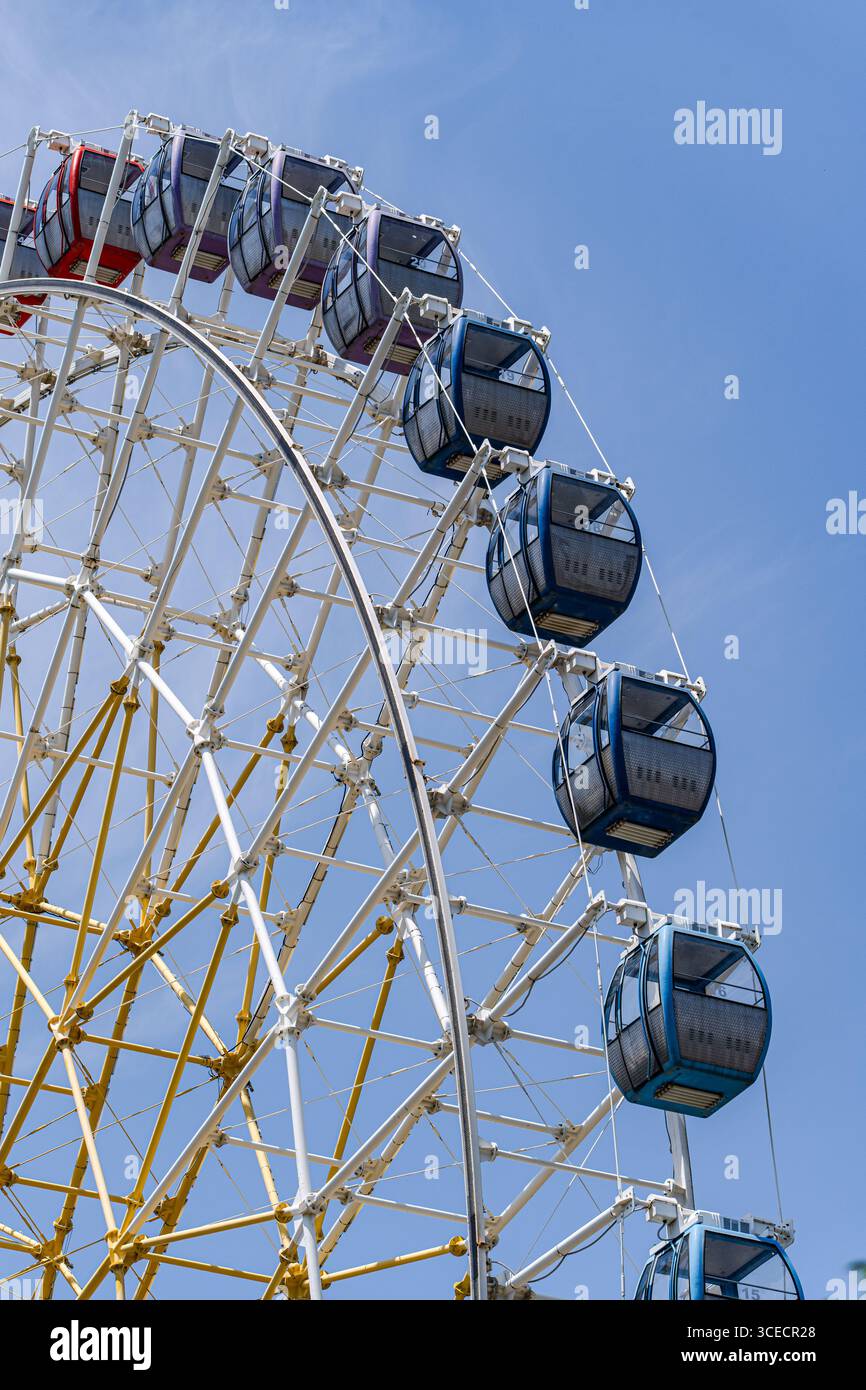 Vue captivante d'une grande roue colorée dominant un ciel bleu vif, illustrant une journée pleine de loisirs et d'aventure dans la ville vibrante Banque D'Images