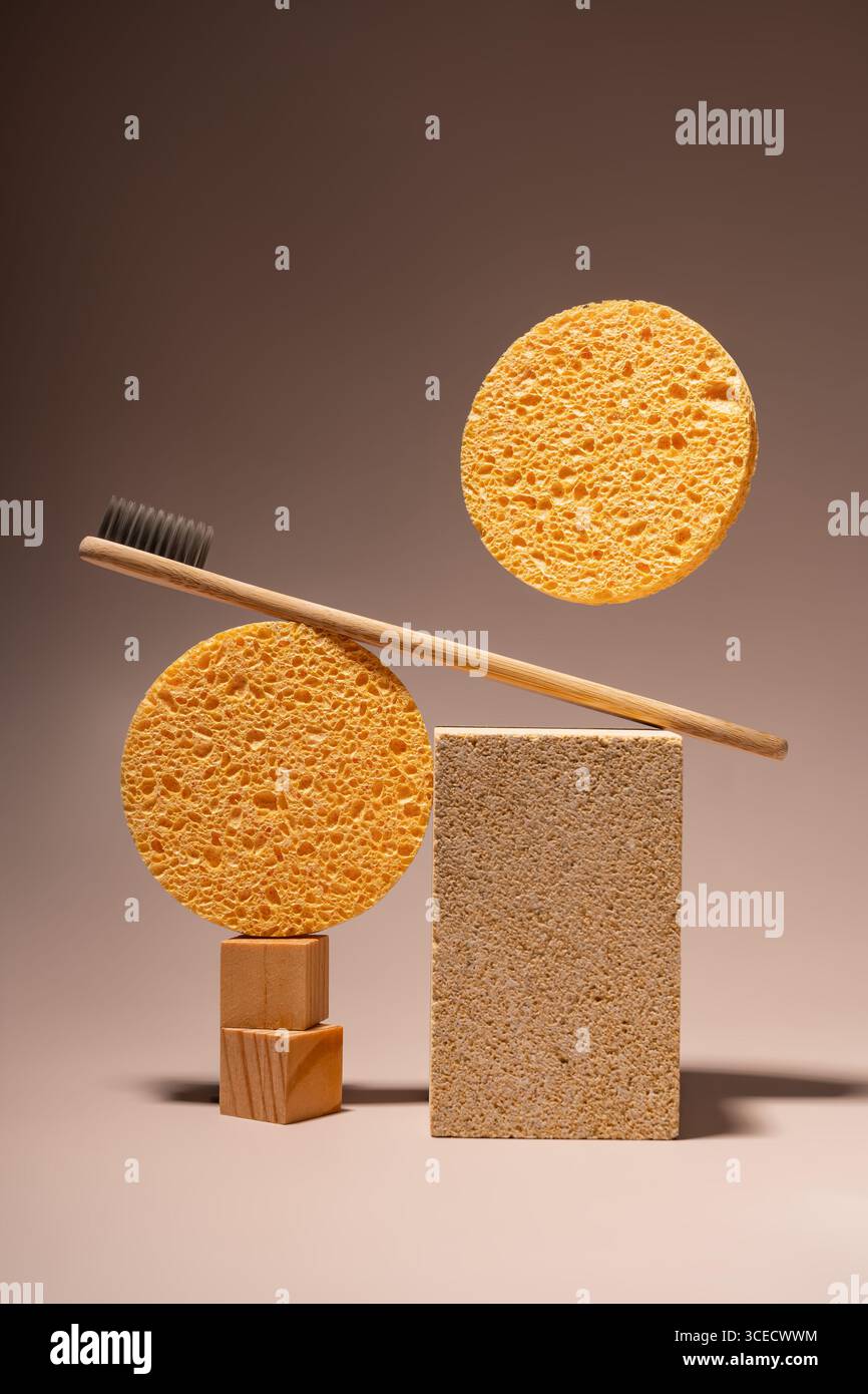 Brosse à dents écologique en bambou repose sur deux éponges circulaires orange. Un bloc de liège rectangulaire complète l'arrangement sur un fond brun minimaliste Banque D'Images