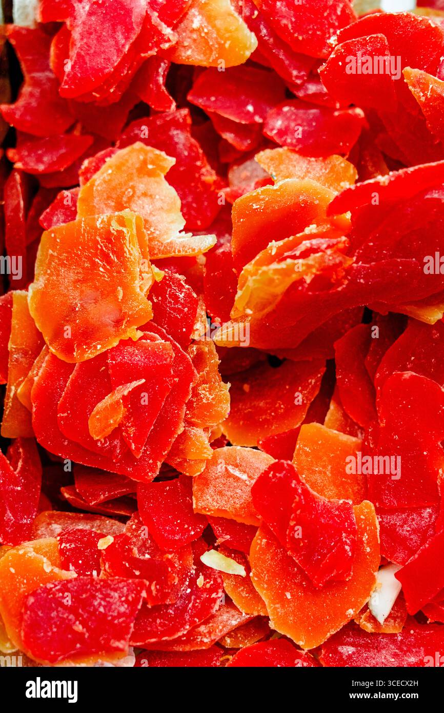 Gros plan de papayes séchées finement tranchées et éclatantes. Les teintes rouge et orange vives créent un contraste saisissant, soulignant leur douceur naturelle et Banque D'Images