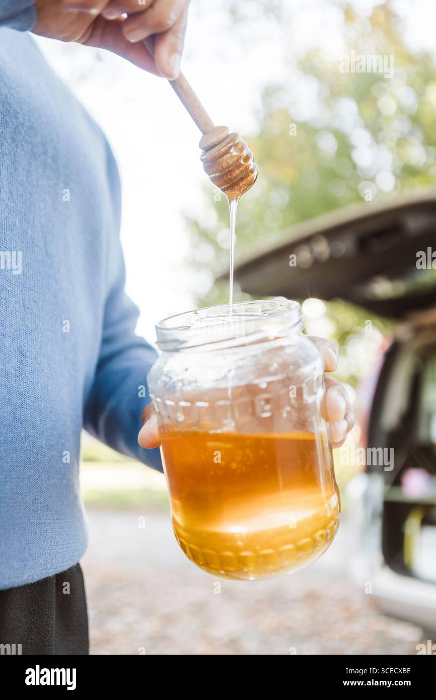 Une femme prend son petit déjeuner avec du miel à l'extérieur de sa camionnette, entourée par les couleurs vibrantes de l'automne en Nouvelle-Zélande. La scène capture un moment de sérénité Banque D'Images