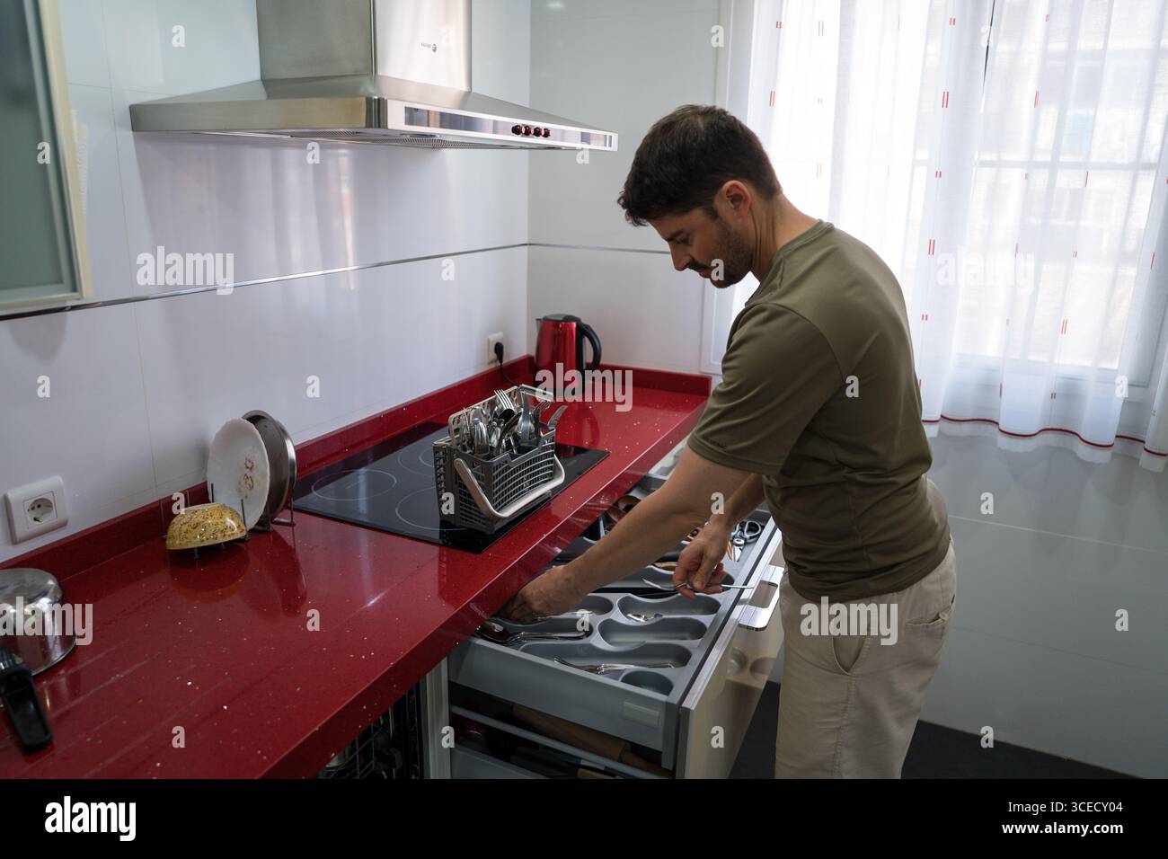Un homme organise des ustensiles dans une cuisine moderne. Il dispose soigneusement les couverts dans un tiroir, faisant preuve d'une gestion efficace du ménage et d'une attention particulière Banque D'Images