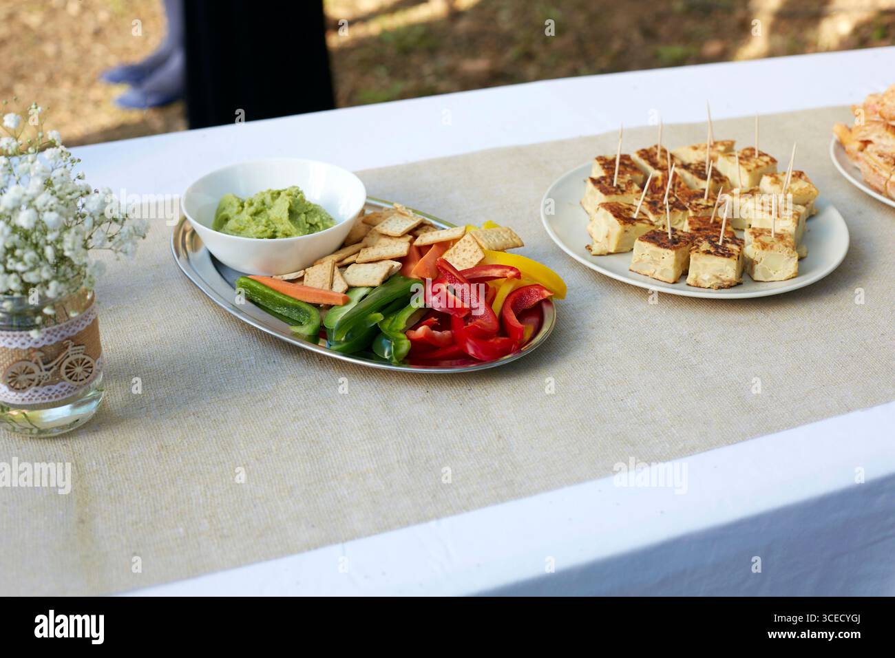 Une table de mariage magnifiquement décorée avec un arrangement floral délicat dans un pot en verre, à côté de plateaux de légumes colorés, guacamole, an Banque D'Images
