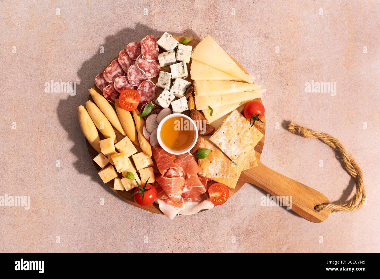 Vue de dessus d'un plateau de fromage élégant avec fromages assortis, viandes, craquelins et tomates cerises sur une planche de bois sur un fond de pierre clair. Banque D'Images
