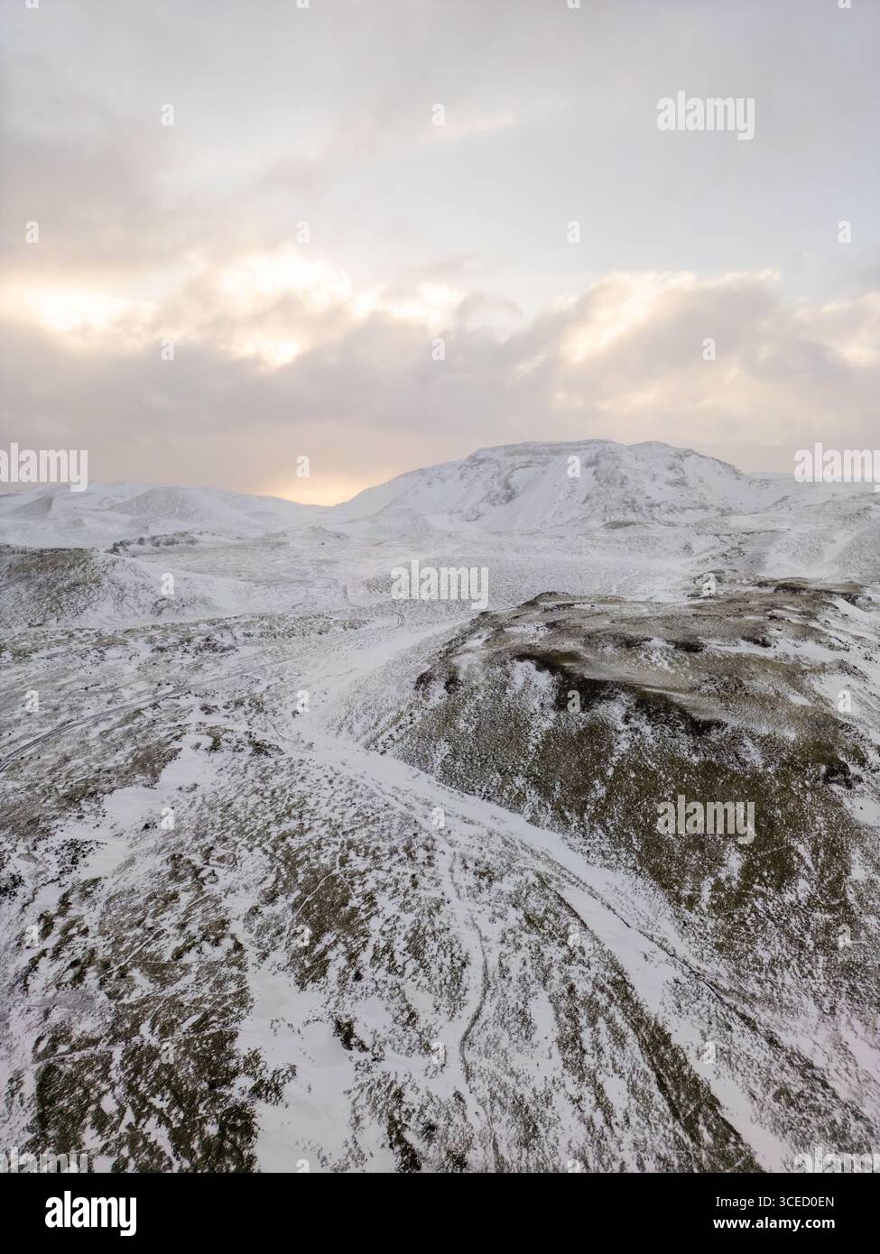 Vue aérienne du paysage hivernal de l'Islande, mettant en valeur les collines enneigées et les montagnes lointaines sous un lever de soleil légèrement éclairé, mettant en évidence les régions reculées et Banque D'Images