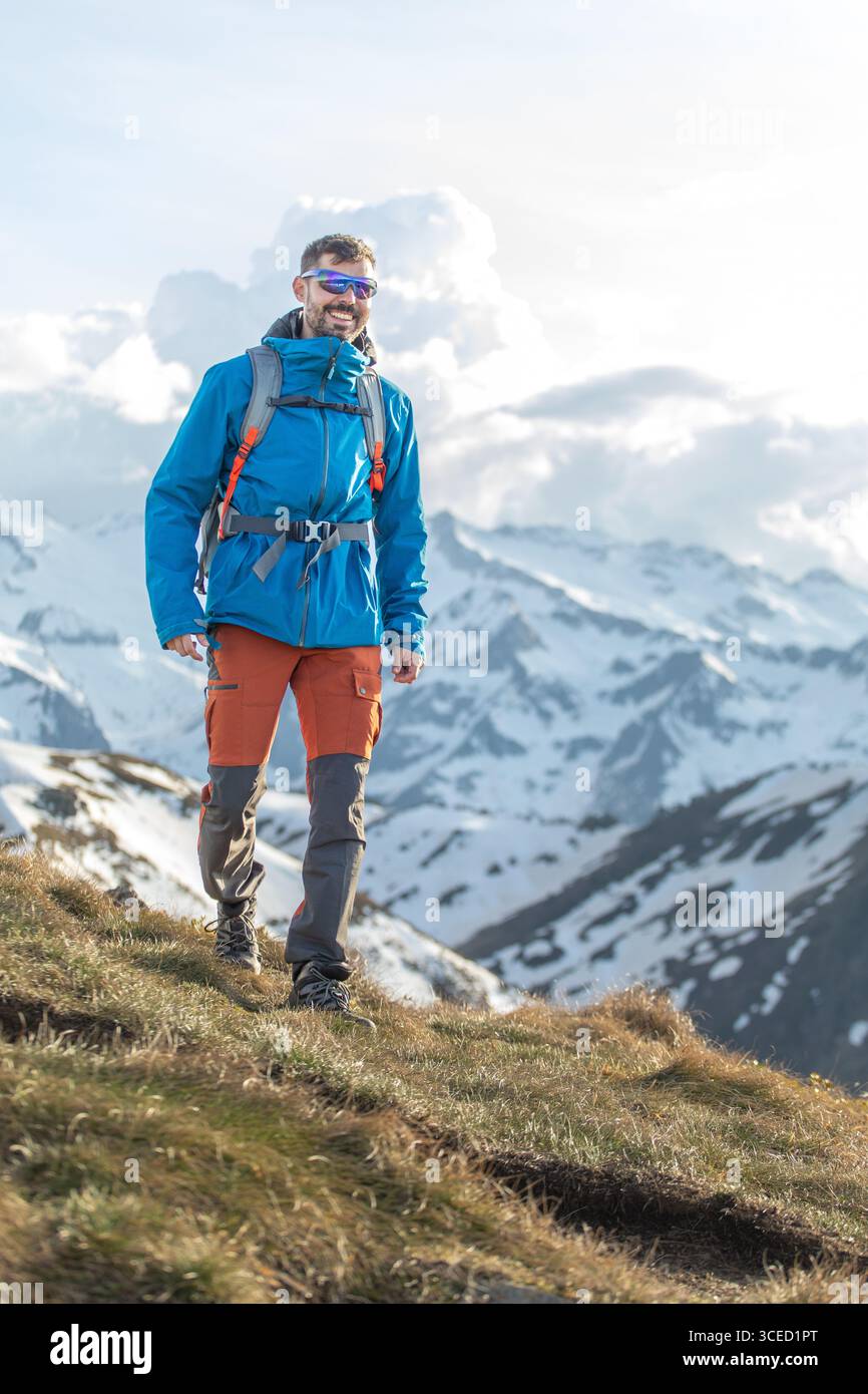 Un homme marche en toute confiance à travers les Pyrénées enneigées, profitant de vues à couper le souffle et de l'air frais de la montagne. Son équipement vibrant se démarque de la sérénité Banque D'Images
