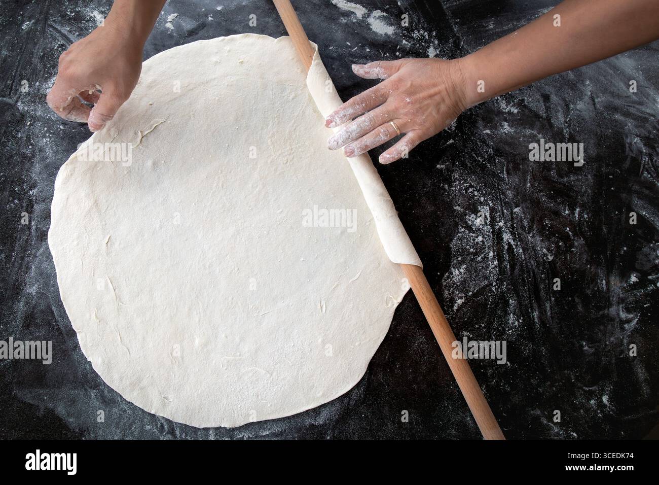 Une vue rapprochée des mains qui déroulent la pâte sur une table en bois. Banque D'Images
